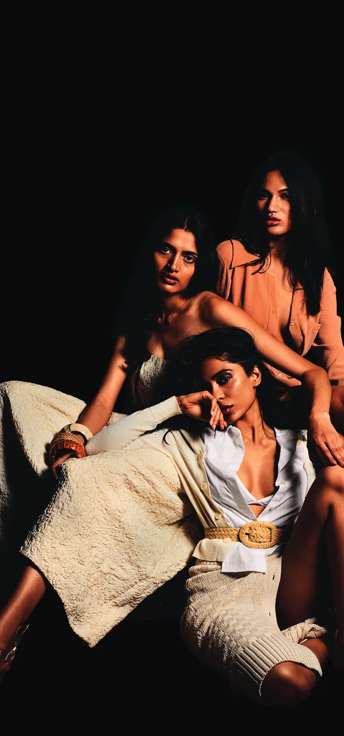 Three women in cream and peach standing together against a black ground, styled for the women's price card cover.